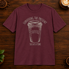 Surviving the Present T-Shirt in Maroon on a dark wood coffee bar