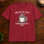 Decaf is Just Performance Art T-Shirt in Antique Cherry Red, close-up on dark wood coffee bar