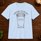 Surviving the Present T-Shirt in Light Blue on a dark wood coffee bar