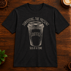 Surviving the Present T-Shirt in Black on a dark wood coffee bar