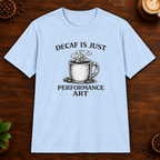 Decaf is Just Performance Art T-Shirt in Light Blue, close-up on dark wood coffee bar